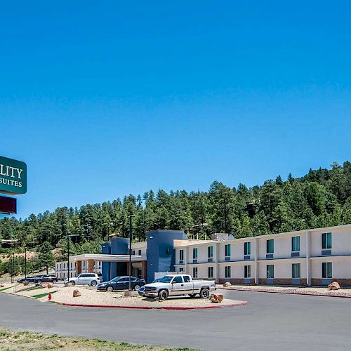 The image shows a Quality Inn & Suites hotel with a parking lot in front, located in a scenic area with forested hills in the background.