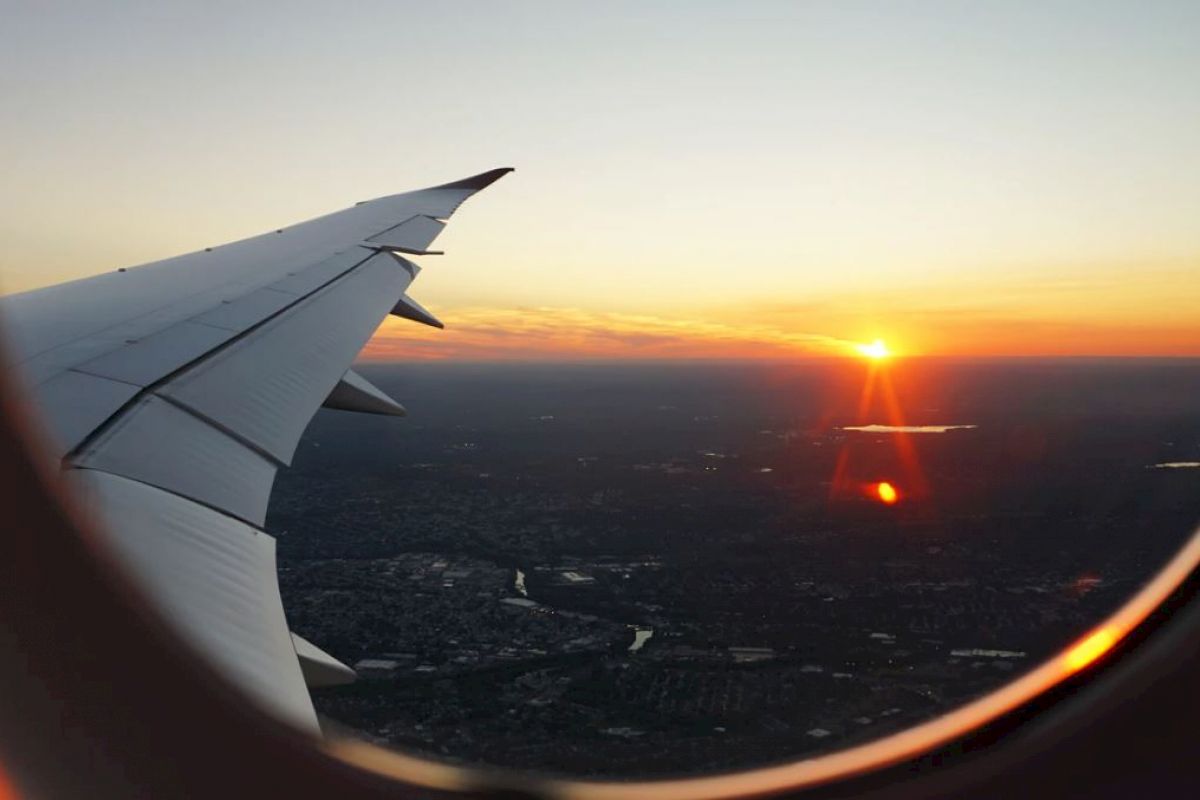 This image shows a view through an airplane window, featuring the wing of the plane and a sunset over a landscape below.