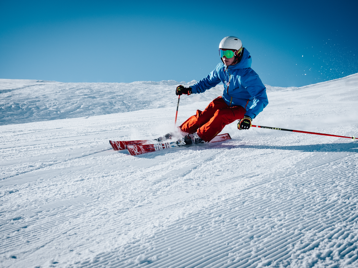 A skier with a helmet and goggles carves down a snowy slope, creating a dynamic spray of snow.